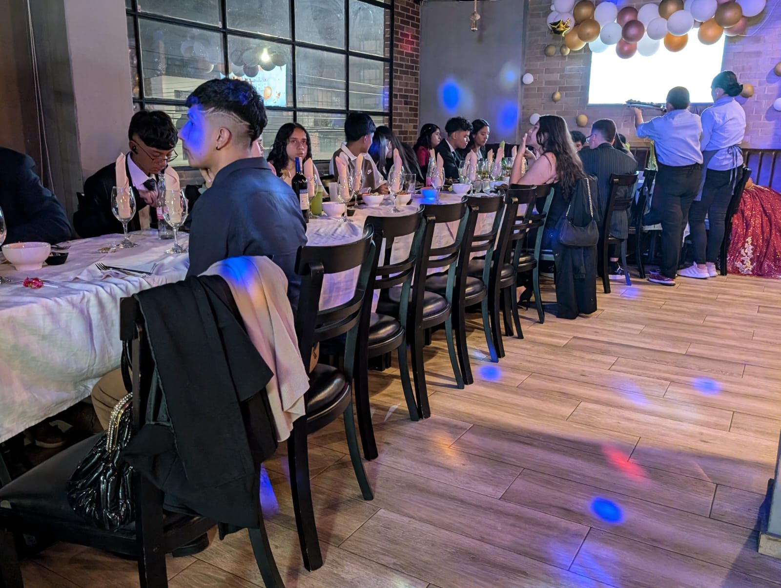 Mesa larga de un evento nocturno con invitados y luces de colores en el piso