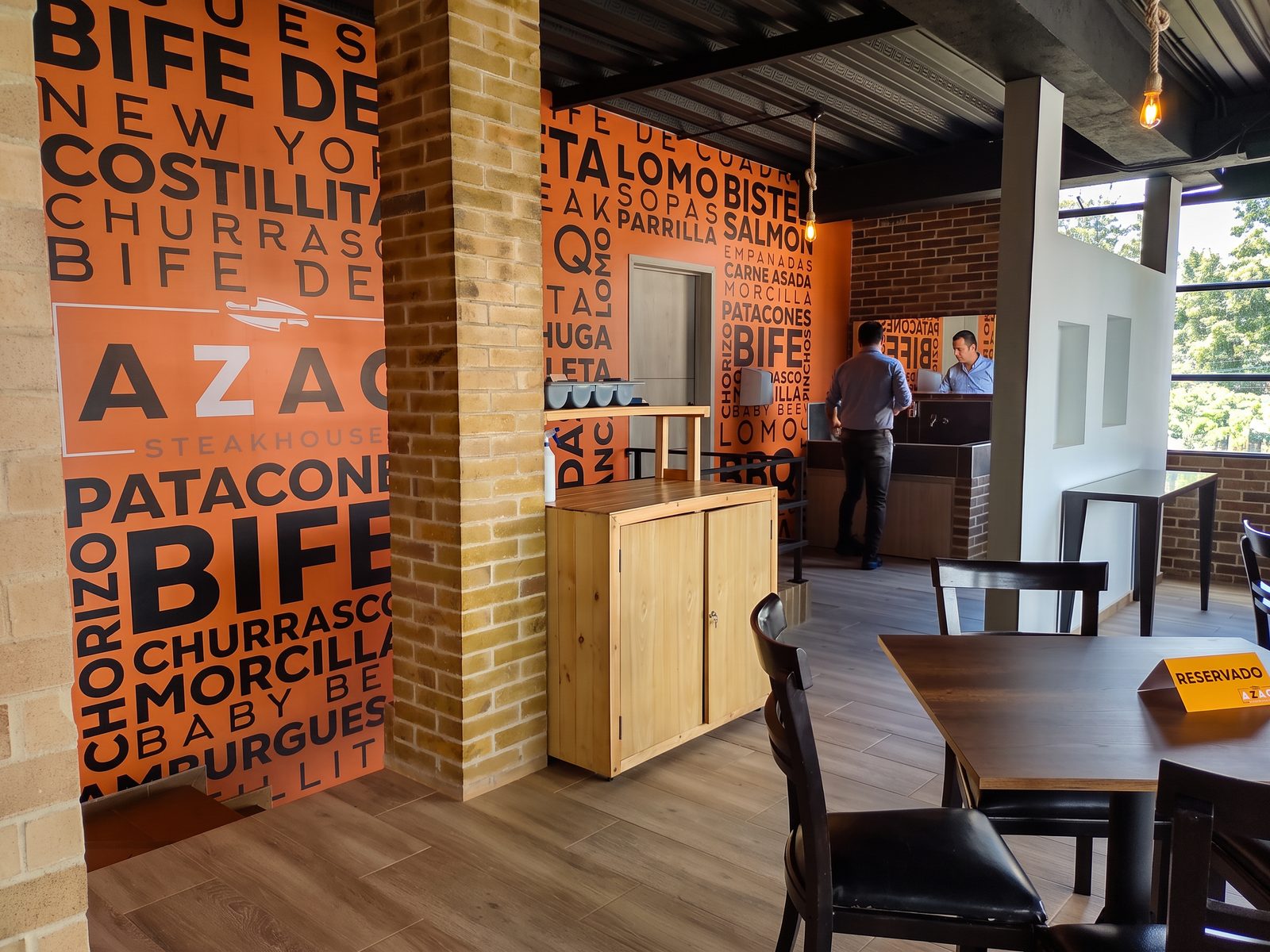 Pared con tipografía naranja de los platos de Azao: bife de chorizo, costillitas, churrasco, morcilla