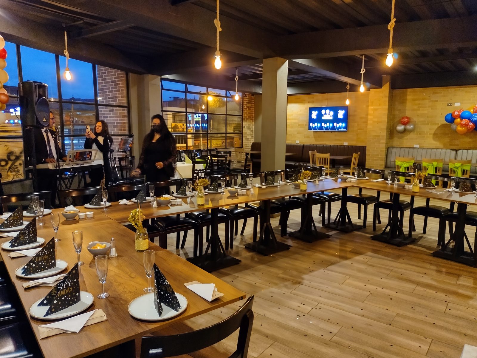 Salón montado en U con servilletas negras y luces colgantes al atardecer